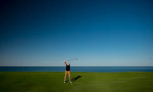 Man Swinging On Golf Course By Sea Wallpaper