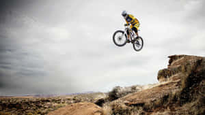 Mountain Biker Mid Air Jump_ Desert Landscape Wallpaper