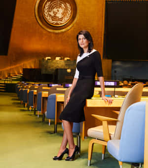 Nikki Haley Confidently Posing Beside A Table In A Stylish Outfit. Wallpaper
