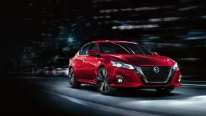 Nissan Altima Driving Through Urban Landscape Wallpaper