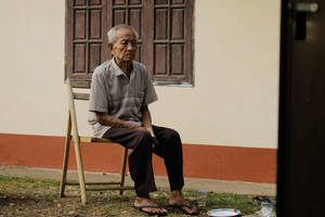 Old Man Sitting In Wooden Chair Wallpaper