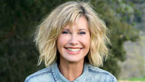 Olivia Newton John Against Blurry Green Trees Wallpaper