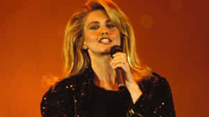 Olivia Newton John Singing In Orange Backdrop Wallpaper