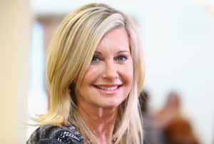 Olivia Newton John Smiling Against Blurry Background Wallpaper