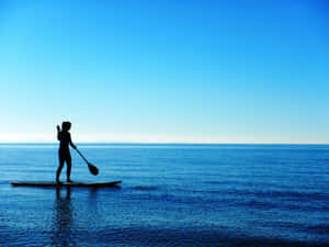 Paddleboarder Gliding Across Calm Waters During A Serene Sunset Wallpaper
