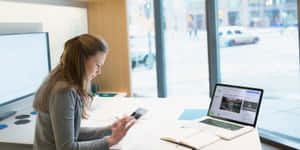 Professional Woman Using Smartphoneat Work Desk Wallpaper