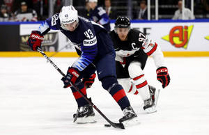 Quinn Hughes Dribbling Hockey Puck In Front Of Player From Team Canada Wallpaper