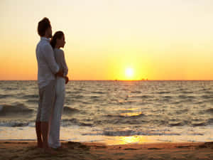 Romantic Couple Enjoying A Sunset Stroll On The Beach Wallpaper