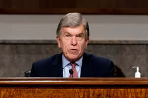 Roy Blunt Thoughtfully Observing From Behind A Ledge Wallpaper