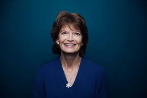 Senator Lisa Murkowski Smiling Against A Blue Aesthetic Background Wallpaper