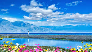 Serene_ Mountain_ Lake_with_ Flowers_and_ Figure Wallpaper