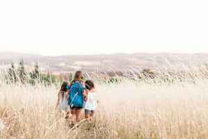 Sisters Embracingin Sunlit Field Wallpaper