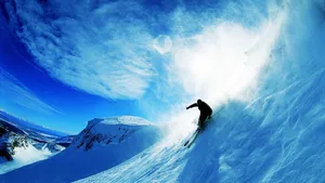 Skier Gliding Downhill Amidst Snowy Mountains Wallpaper