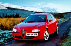 Sleek Red Alfa Romeo 147 In Picturesque Landscape Wallpaper