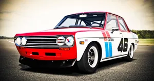 Sleek Red Datsun On A Scenic Road Wallpaper