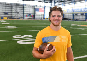 Smiling Athlete Holding Football Indoors Wallpaper