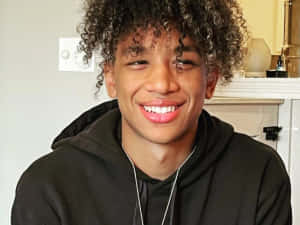Smiling Curly Haired Boyin Black Hoodie Wallpaper