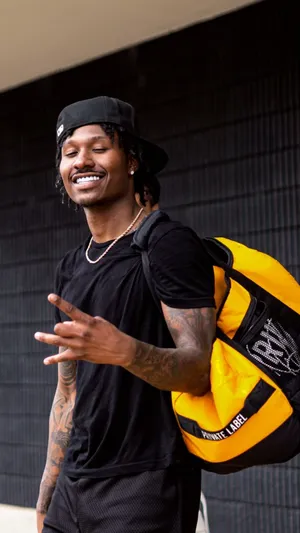 Smiling Manwith Black Capand Yellow Backpack Wallpaper