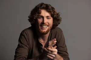 Smiling Manwith Curly Hairand Brown Shirt Wallpaper