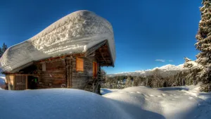 Snow Covered Wooden Cottagein Mountain Setting Wallpaper