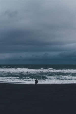 Solitary_ Figure_on_ Stormy_ Shoreline Wallpaper