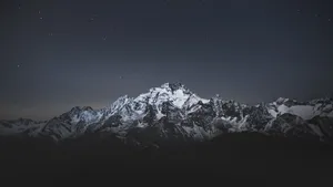 Stand Tall And Admire The Beauty Of The Night Sky And A Majestic Mountain. Wallpaper