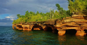 Sunlit_ Cliffside_ Over_ Water Wallpaper