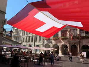 Swiss_ Flag_ Over_ Lausanne_ Street_ Scene Wallpaper