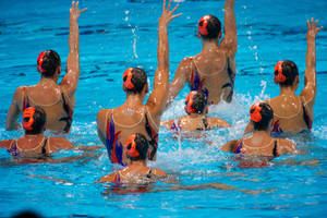 Synchronized Swimmers With Hands Up In Perfect Harmony Wallpaper