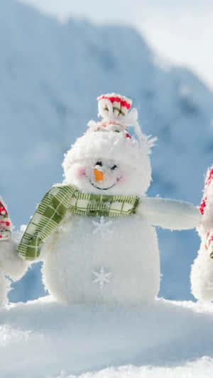 Three Snowmen Standing In The Snow With A Mountain In The Background Wallpaper