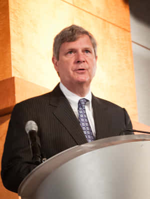 Tom Vilsack Speaking On Podium Wallpaper