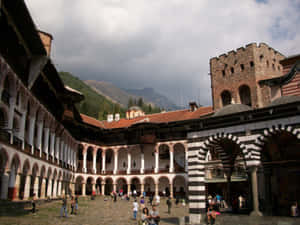 Tourists Exploring The Majestic Rila Monastery In Bulgaria Wallpaper