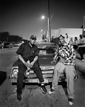 Two Men Sitting On The Side Of A Car At Night Wallpaper