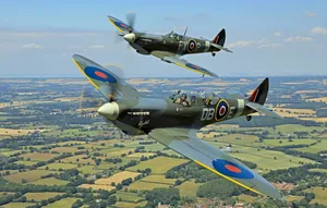 Two Old War Planes Flying Over A Field Wallpaper