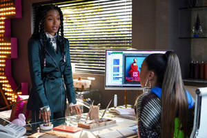 Two Women Standing At A Desk In Front Of A Computer Wallpaper