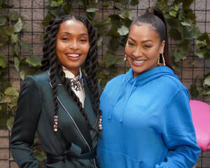 Two Women Standing Next To Each Other In Front Of A Wall Wallpaper