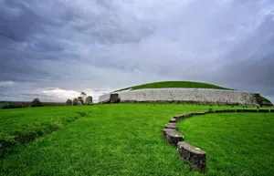 Vibrant Newgrange Passage Tomb With Stormy Cloud Wallpaper