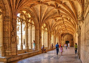 Visitors Exploring The Historic Mosteiro Dos Jeronimos In Lisbon, Portugal. Wallpaper