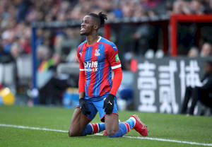 Wilfried Zaha Kneeling On Football Field Wallpaper