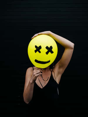 Woman Holding A Yellow Smiley Face Balloon Wallpaper