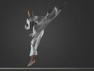 Young Martial Artist Striking A High Kick Pose In A White Training Uniform Wallpaper