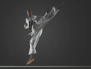 Young Martial Artist Striking A High Kick Pose In A White Training Uniform Wallpaper
