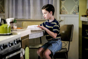 Young Sheldon Readingat Kitchen Counter Wallpaper